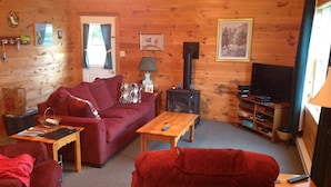 Un acogedor interior de cabaña con detalles de madera, un sofá, una mesa de centro, un televisor y una chimenea.