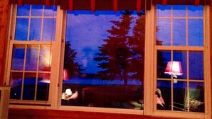 Una cabaña de madera con dos ventanas, cada una con vistas a un paisaje boscoso.