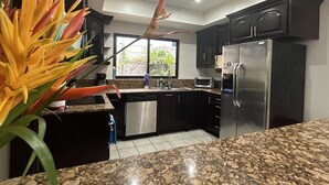 A modern kitchen with dark cabinetry, a stainless steel refrigerator, and a granite countertop.