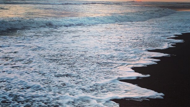 A beach with waves and a sunset.