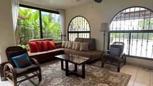 A living room with a sofa, chairs, a coffee table, and a view of greenery outside.