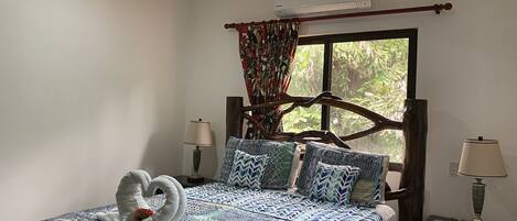 Un dormitorio con cama, ventilador de techo, aire acondicionado, ventana con cortinas y dos lámparas de noche.