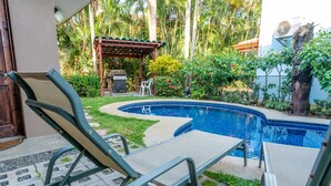 A swimming pool with lounge chairs, a barbecue area, and lush greenery.