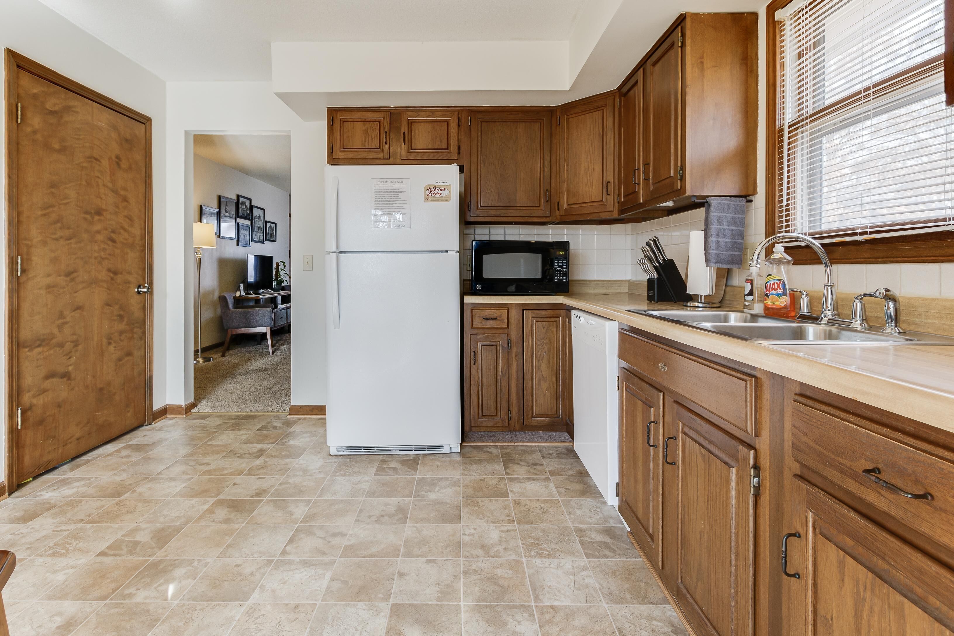 A kitchen with wooden cabinets, a refrigerator, a microwave, and a sink.