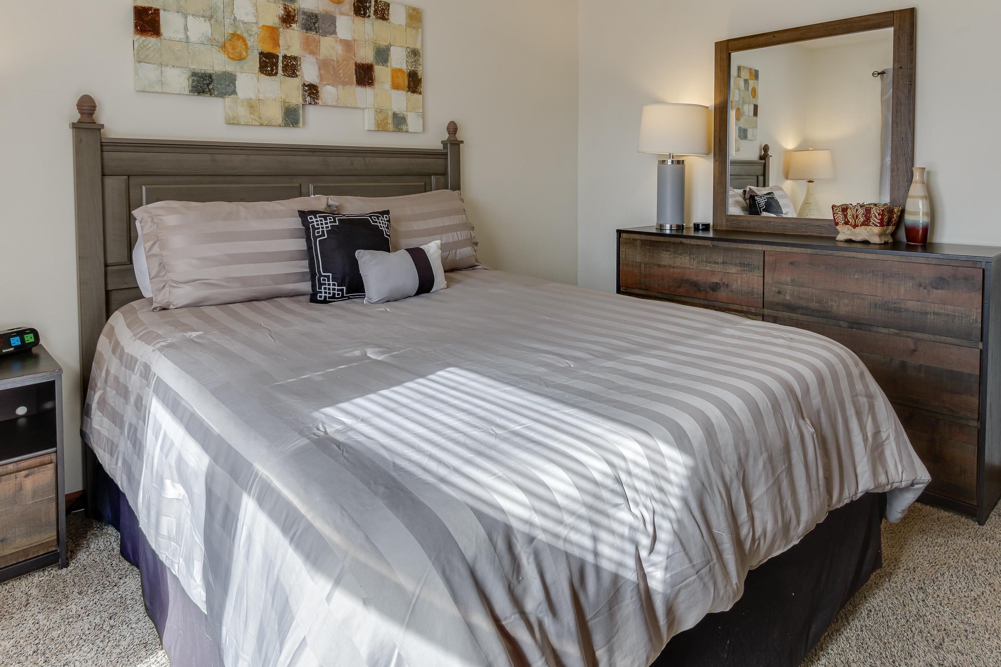 A neatly made bed with a striped bedspread, a wooden headboard, and a bedside table with a lamp.