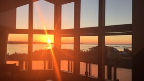 Et værelse med store vinduer med udsigt til en solnedgang over vandet.