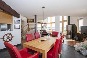 A modern kitchen with a wooden table and red chairs, a staircase, and a large window.