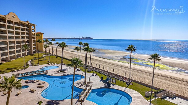 A hotel with a pool area, palm trees, and a beach view.