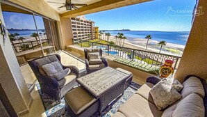 A balcony with a view of the beach and ocean, furnished with a sofa, chairs, and a coffee table.
