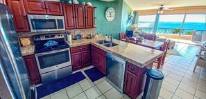 A kitchen with a microwave, oven, and sink. There is a dining area with a table and chairs. A clock is on the wall. - Sonoran Spa W506 - 2 BR Next to the Pool, High Speed Wi-Fi - Beachfront Upper Floor Luxury Condo (Puerto Peñasco)