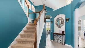 A staircase with wooden railings and beige carpet leading to a hallway with teal walls and a decorative mirror. - Take a look at the reviews! Great value! An awesome place!!! Sleeps up to 16. (Kissimmee)