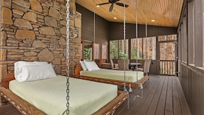 A wooden deck with two beds suspended by chains, a stone wall, and a ceiling fan. - Hot tub, Rustic Elegance, In and outside fireplaces, Private, 10 miles to AVL. (Fairview)