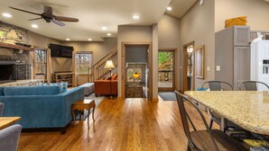 A spacious living area with a fireplace, a blue sofa, a dining table, and a kitchen with a refrigerator and cabinets. - Hot tub, Rustic Elegance, In and outside fireplaces, Private, 10 miles to AVL. (Fairview)