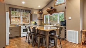 A kitchen with a central island, wooden chairs, a stove, and a window with a view of trees. - Hot tub, Rustic Elegance, In and outside fireplaces, Private, 10 miles to AVL. (Fairview)