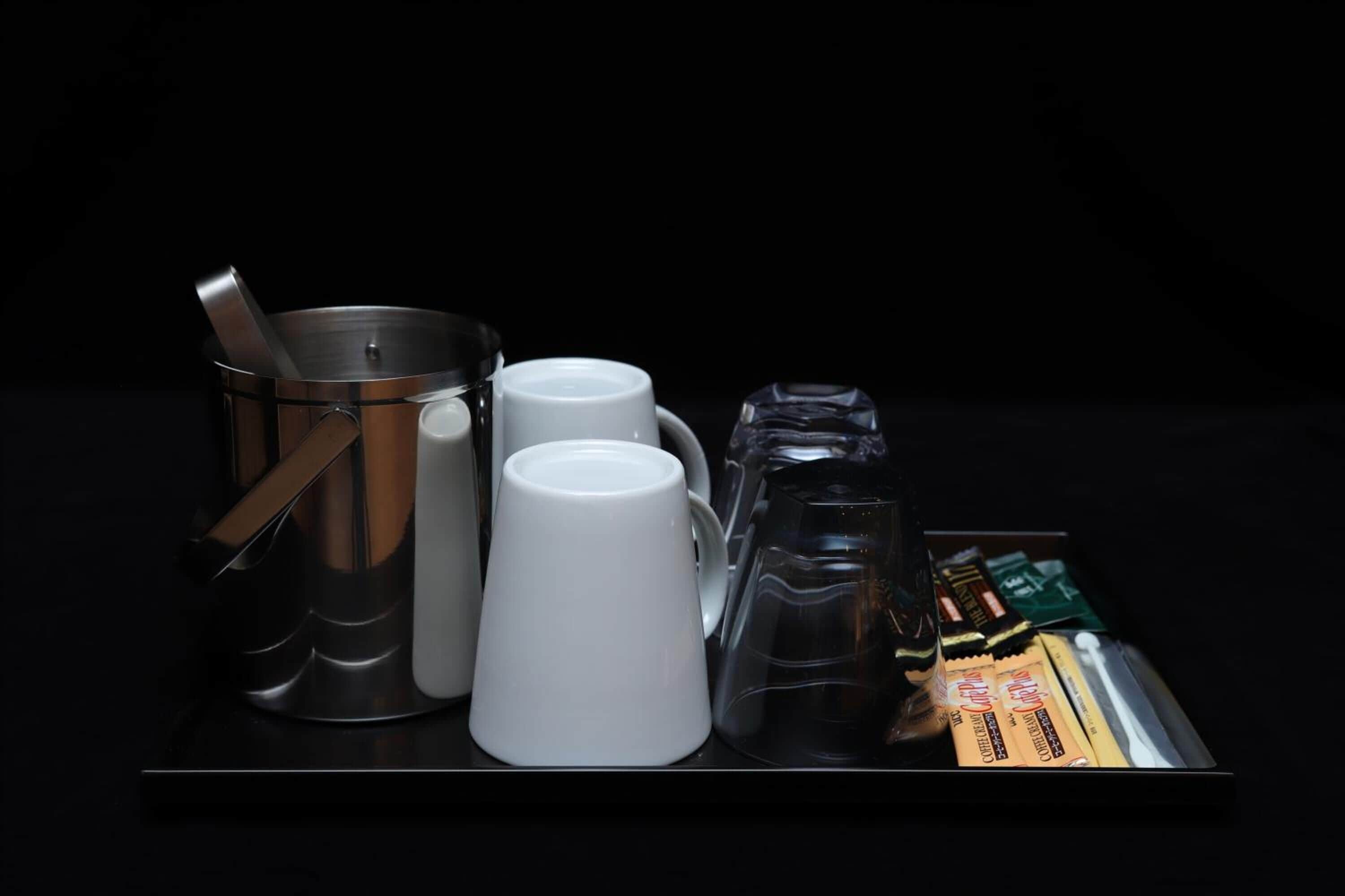 Una bandeja con una cafetera de acero inoxidable, dos tazas blancas, una jarra de vidrio y una caja de barras de chocolate.