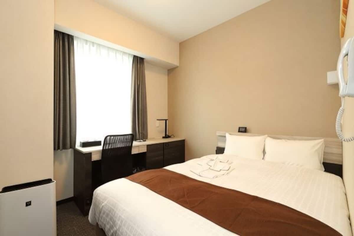 A hotel room with a bed, desk, chair, and a telephone.