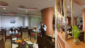 A modern restaurant with round tables, red cushioned chairs, and a waiter attending to a table. - Hotel Sewa Grand Faridabad (Faridabad)