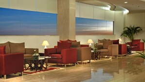 A modern lobby with red sofas, a glass coffee table, and a large abstract painting on the wall. - Hotel Sewa Grand Faridabad (Faridabad)