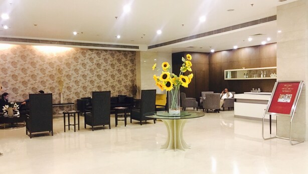 A hotel lobby with a reception desk, seating area, and a decorative vase with sunflowers. - Hotel Sewa Grand Faridabad (Faridabad)