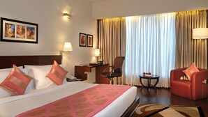 A hotel room with a large bed, two chairs, a desk, and a TV. - Hotel Sewa Grand Faridabad (Faridabad)