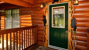 A log cabin with a green door, wooden railing, and bear decorations. - Making Memories-Theater Room, Pool Table, Arcade, Bear Wood Carvings, Hot Tub (Sevierville)