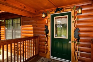A log cabin with a green door, wooden railing, and bear decorations. - Making Memories-Theater Room, Pool Table, Arcade, Bear Wood Carvings, Hot Tub (Sevierville)