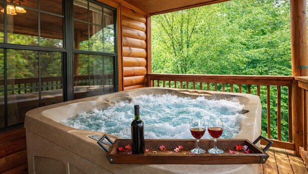 A hot tub with a wooden deck, a bottle, and glasses on a tray. - Making Memories-Theater Room, Pool Table, Arcade, Bear Wood Carvings, Hot Tub (Sevierville)