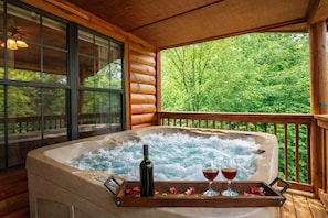 Ein Whirlpool mit einer Holzterrasse, einer Flasche und Gläsern auf einem Tablett.