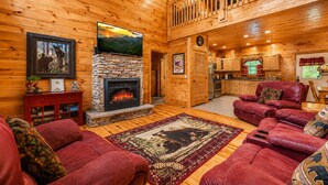 A log cabin interior with a stone fireplace, red leather sofas, a wooden dining area, and a kitchen. - Making Memories-Theater Room, Pool Table, Arcade, Bear Wood Carvings, Hot Tub (Sevierville)