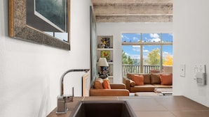 A modern kitchen with a large sink, a dining area with a sofa and table, and a view of the outdoors through a window.
