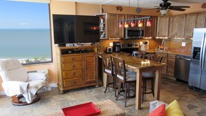 Una cocina con vista al océano, armarios de madera, una mesa de comedor y una bandeja roja sobre un banco acolchado.