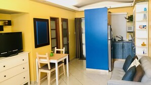 A compact living space with a television, a dining table with chairs, a sofa, a kitchen area with a sink, and a blue partition. - Beautiful Condo -Ocean View, Best Location, Pool, A Few Steps to All You Want (Santurce)