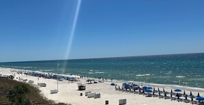 Una spiaggia con file di ombrelloni blu e lettini, una torretta di salvataggio e una vista libera sull'oceano.