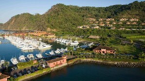 A marina with multiple boats docked, a golf course, and residential buildings on a hillside.