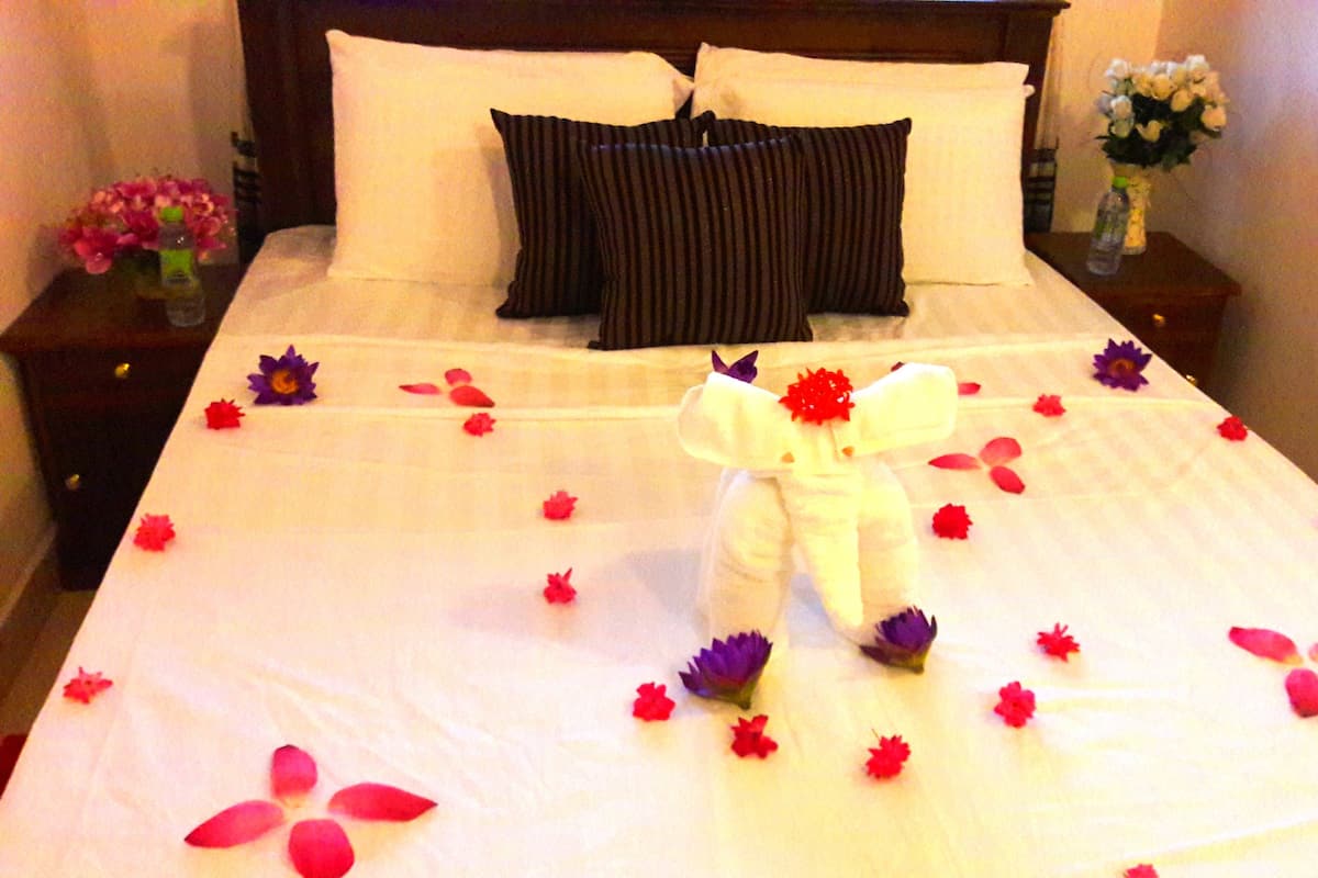 A neatly made bed with a white comforter, pillows, and a decorative arrangement of flowers and petals.