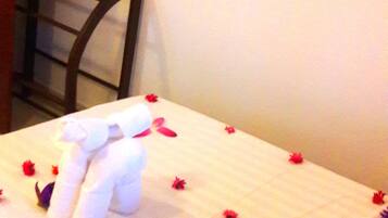 Un lit bien fait, recouvert d’une couverture blanche et parsemé de pétales de fleurs rouges.