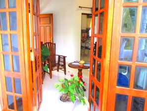Una puerta de madera abierta que da a una habitación con una silla, una mesita y una planta en maceta.