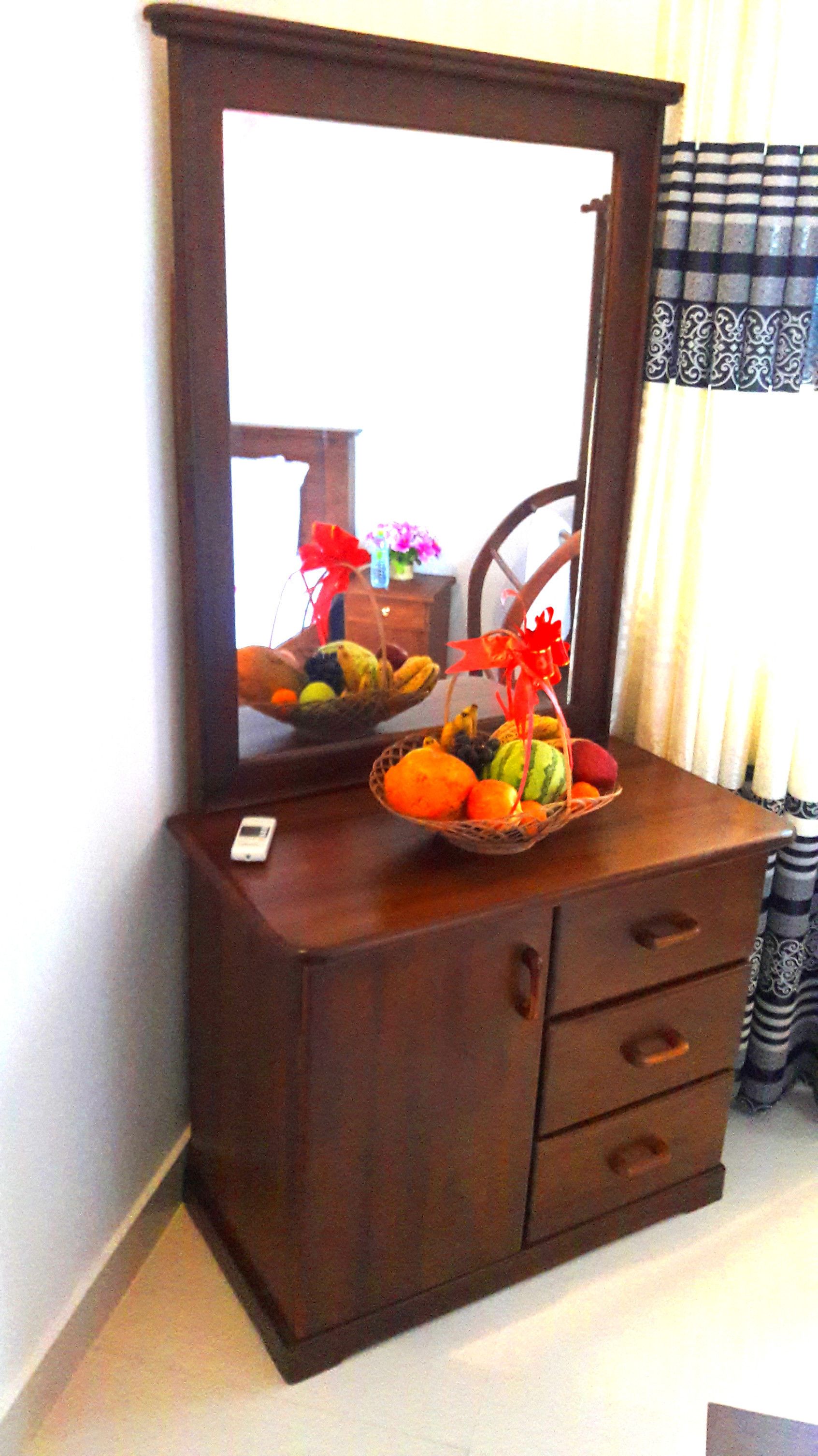 A wooden dresser with a mirror, a basket of fruit, and a small vase with flowers.