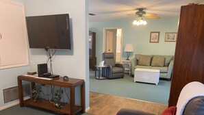 Una sala de estar con televisión, una mesa de madera, un sofá gris y un ventilador de techo.
