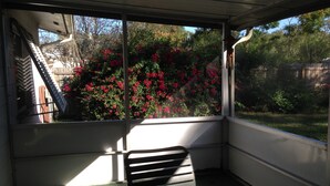Un porche cubierto con una silla y vistas a un jardín con flores rojas.
