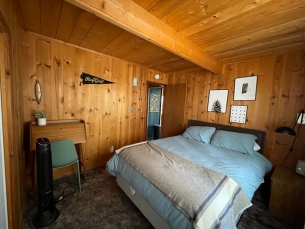A wooden-paneled room with a bed, a desk, and a chair.