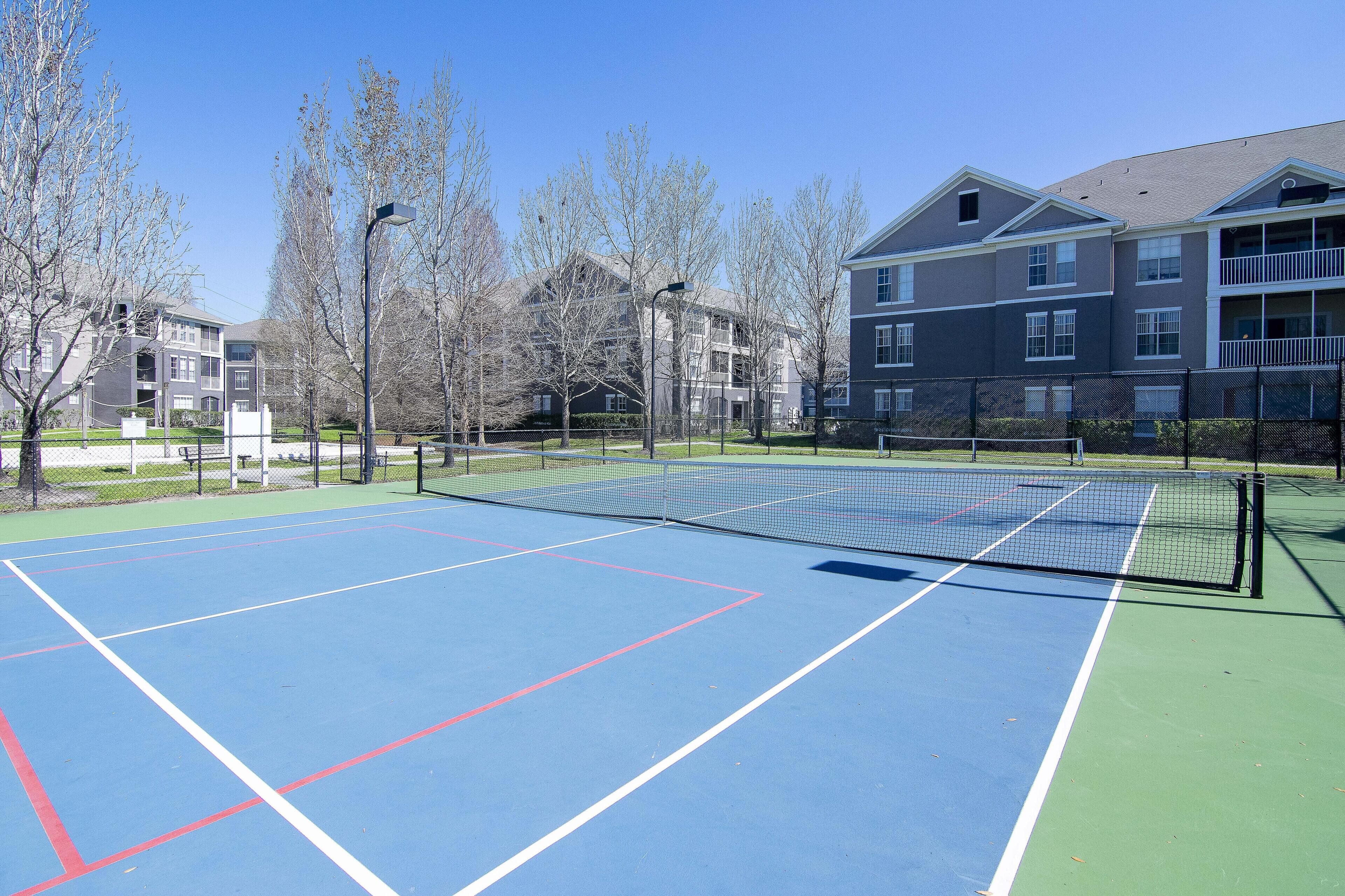 A tennis court with a net, surrounded by trees and buildings.