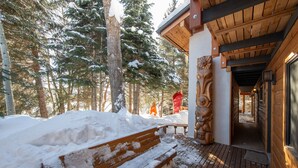 Eine hölzerne Bank mit Schnee, ein Holzterrasse und ein Gebäude mit Holzfassade und einer Tür.