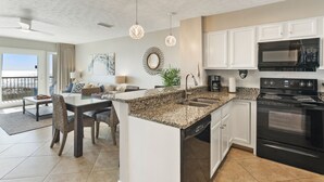 A modern kitchen with granite countertops, white cabinets, a black stove, and a dining area with a glass table and chairs.
