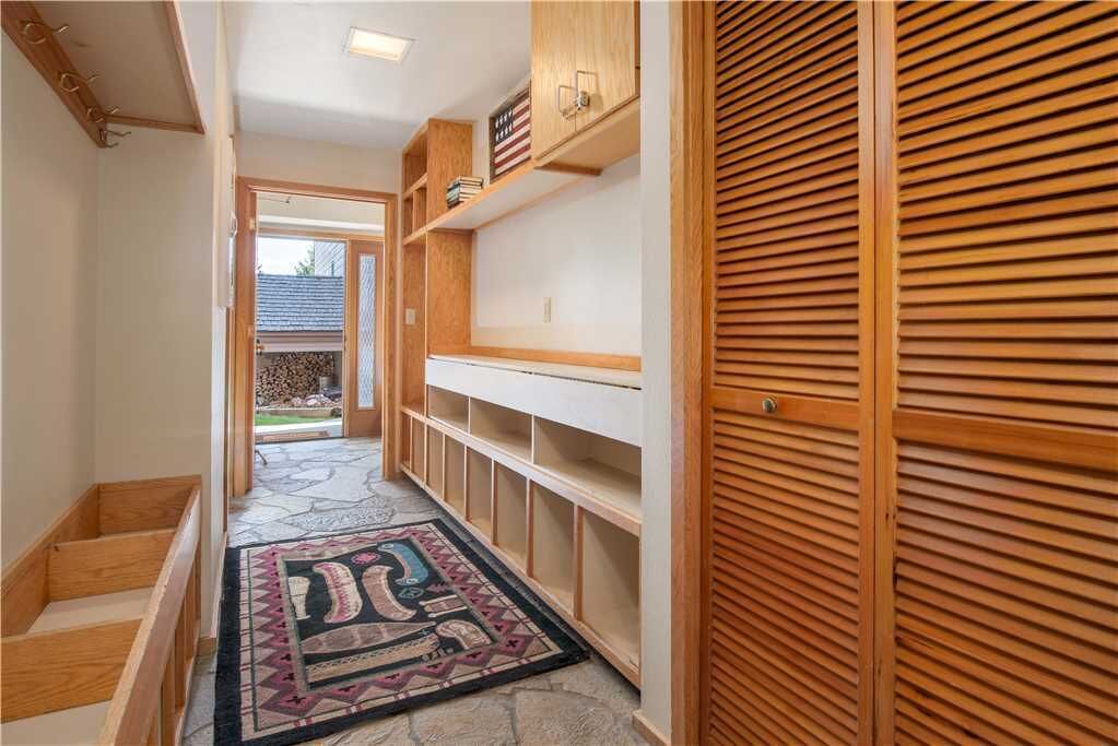 A hallway with wooden shelves, a patterned rug, and a view into a backyard.