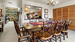 Un espace repas comprenant une grande table et des chaises en bois, un lustre et une vue sur l’extérieur.