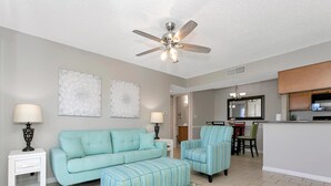 A living room with a sofa, ottoman, and chairs, a dining area with a table and chairs, and a kitchen with cabinets and a countertop. - Lake Front - Ground Level - 2 bedroom 2 bath (Brandon)