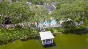 A house with a swimming pool surrounded by trees, a dock extending into a pond, and a covered deck area. - Lake Front - Ground Level - 2 bedroom 2 bath (Brandon)