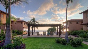 A courtyard with a pergola, palm trees, and a view of the ocean. - Beautiful serene apartment-saltwater pool, gardens, 200 feet from the beach! (Troncones)