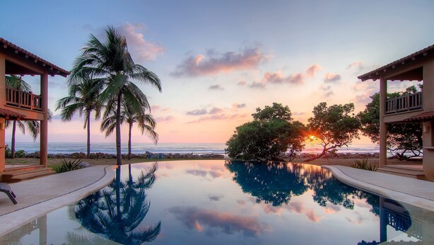 An infinity pool reflecting palm trees and the sunset, with a view of the ocean and beach. - Beautiful serene apartment-saltwater pool, gardens, 200 feet from the beach! (Troncones)